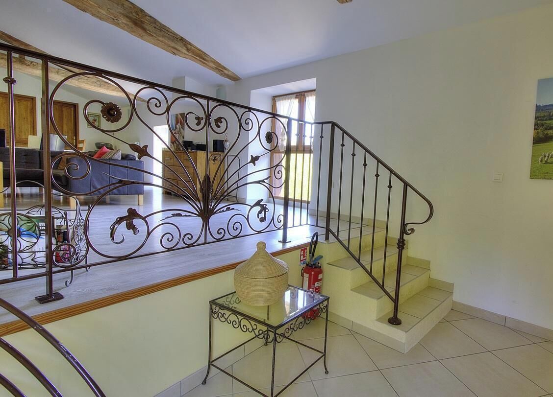 Un escalier orné de rampes en métal ouvragé, une petite table surmontée d’un panier en osier et un extincteur.