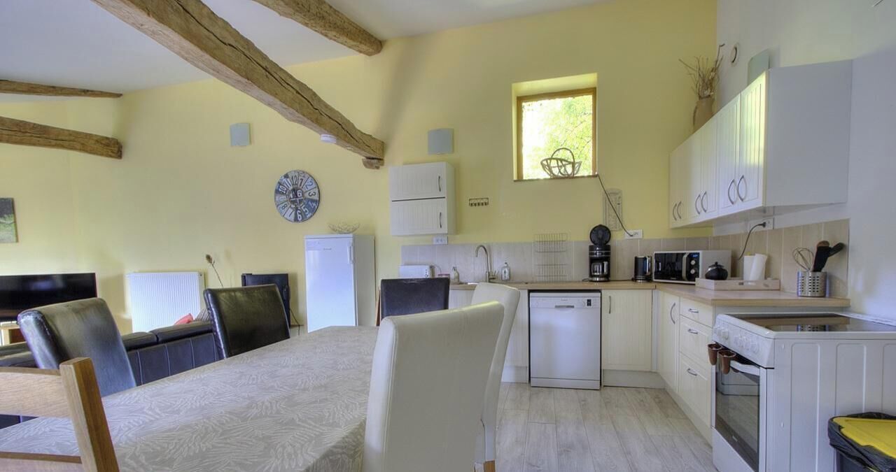 A kitchen with white cabinets, a microwave, a coffee maker, and a sink. There is a dining table with chairs and a clock on the wall.