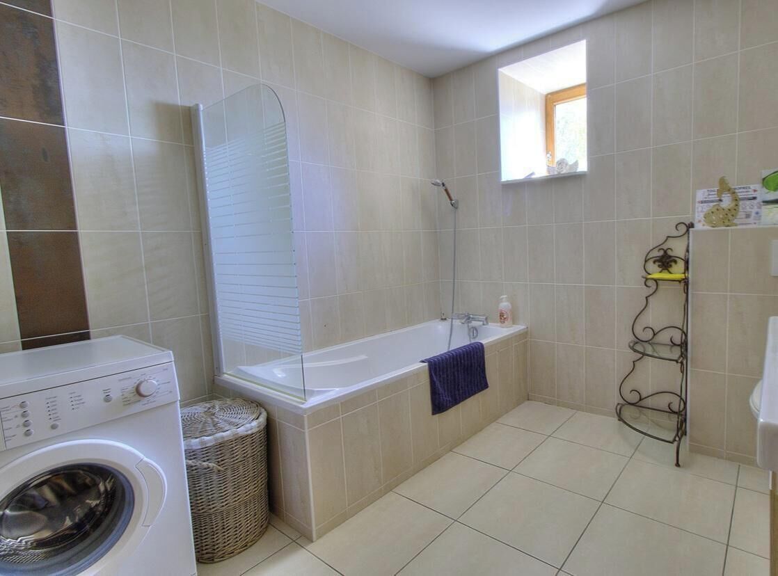 Een badkamer met een wasmachine, een bad, een douche, een klein raam en een metalen plank.
