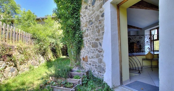 A stone building with a wooden fence, a garden with raised beds, and a balcony with a metal railing.