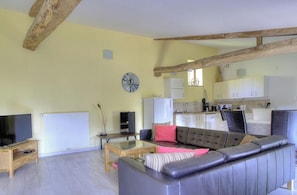 A living room with a sofa, coffee table, TV, and a kitchen area in the background.