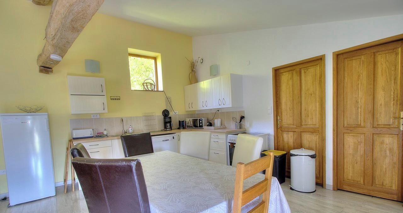 A compact kitchen with a dining table, chairs, a refrigerator, cabinets, and a window.
