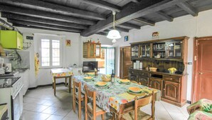 A dining area with a table set for four, surrounded by wooden chairs. There is a kitchen area with a refrigerator, stove, and cabinets. The room has a tiled floor and a wooden ceiling with exposed beams. - 1 bedroom gorgeous apartment in Codivara (Codivara)