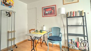 A dining area with a table, chairs, a bookshelf, and artwork on the walls. - Studio Berthelot 20 - Oullins (OULLINS)