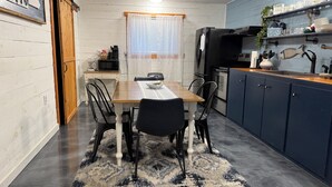 Una cocina compacta con una mesa de comedor, sillas, microondas, refrigerador y alacenas.