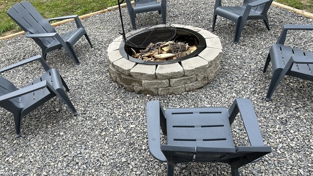 Un hogar circular de piedra rodeado por seis sillas Adirondack.