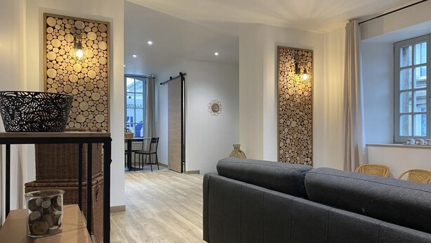 Ein modernes Wohnzimmer mit einem grauen Sofa, einem Esstisch mit Stühlen und einer Wand mit kreisförmigen Holzmustern.