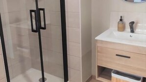 Ein modernes Badezimmer mit einer gläsernen Duschkabine, einem weißen Waschbecken mit Spiegel und einer Holz-Kommode.