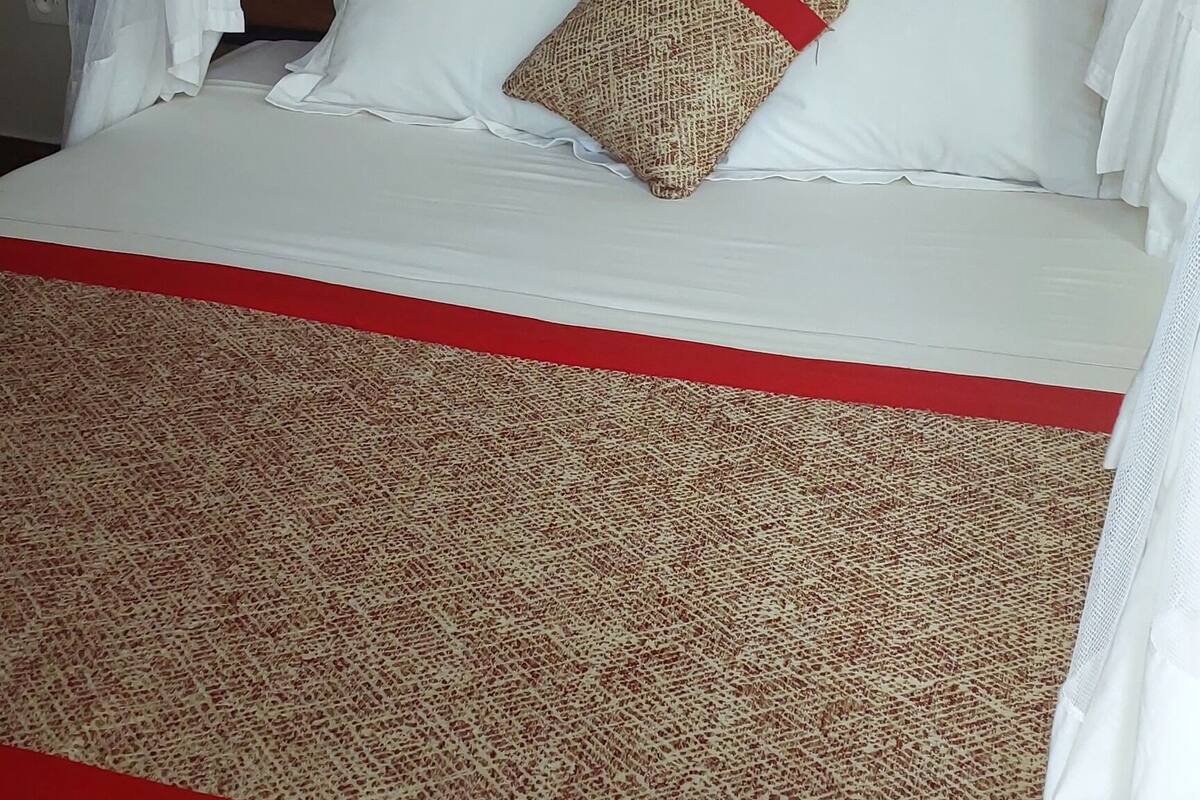 A bed with a canopy, white bedding, a patterned throw, and a red accent.