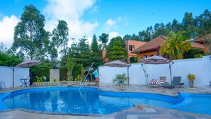 A swimming pool with a tiled deck, surrounded by outdoor furniture and umbrellas. - Andasibe Cyperus Hotel (Andasibe)