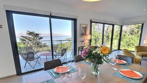 Un coin repas avec une table dressée pour quatre personnes, de grandes portes-fenêtres coulissantes et une vue sur la mer.