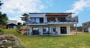 Ein modernes, zweistöckiges Haus mit Balkon, überdachter Terrasse und gepflegtem Rasen.