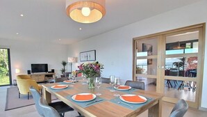 Une salle à manger moderne avec une table en bois dressée pour quatre personnes, un téléviseur et une grande fenêtre.
