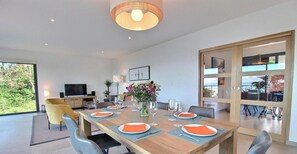 A modern dining room with a wooden table set for four, a television, and a large window.