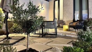 Un patio al aire libre con un árbol pequeño, un banco y una mesa.