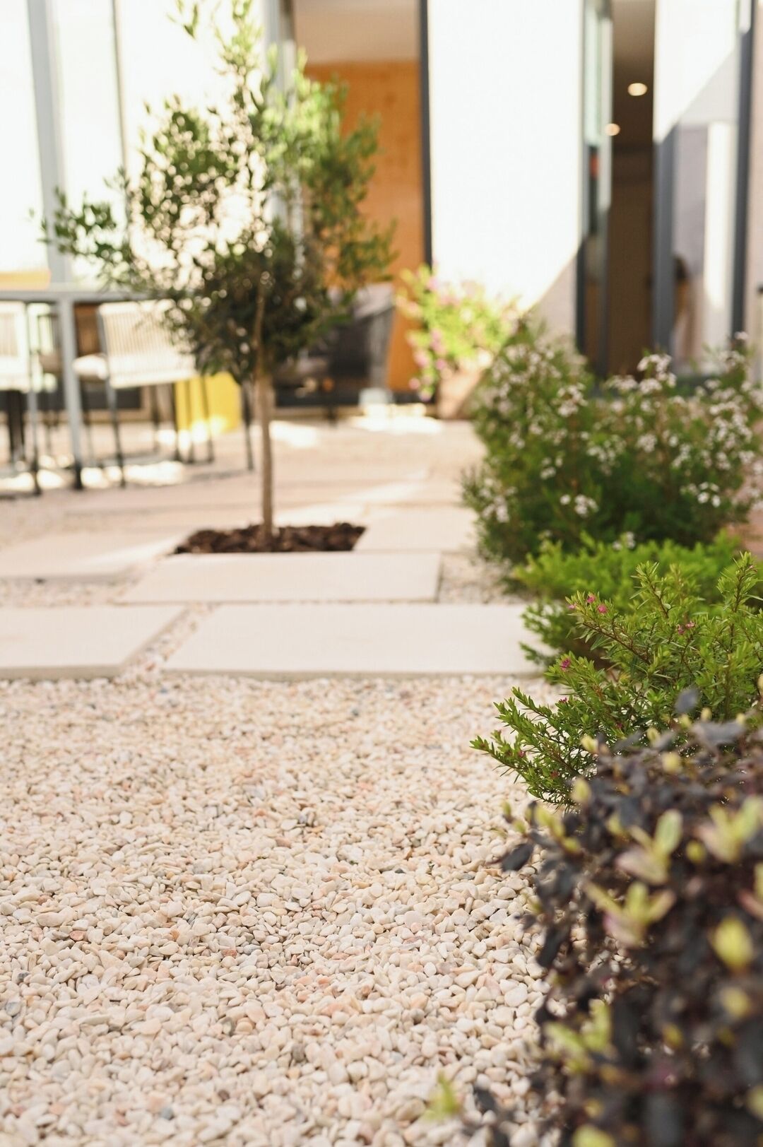 A pathway with pebbles leading to a seating area with tables and chairs.