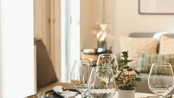 A dining table set with plates, cutlery, and wine glasses, with a vase of greenery and a framed picture on the wall.