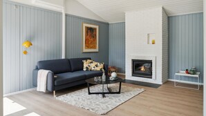 A living room with a dark blue sofa, a white fireplace, and a painting on the wall. - Beautiful home in Hornbæk with WiFi (Hornbæk)