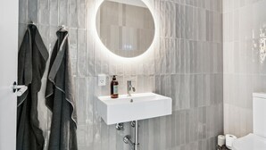 A bathroom with a white sink, a round mirror, and grey tiled walls. - Beautiful home in Hornbæk with WiFi (Hornbæk)