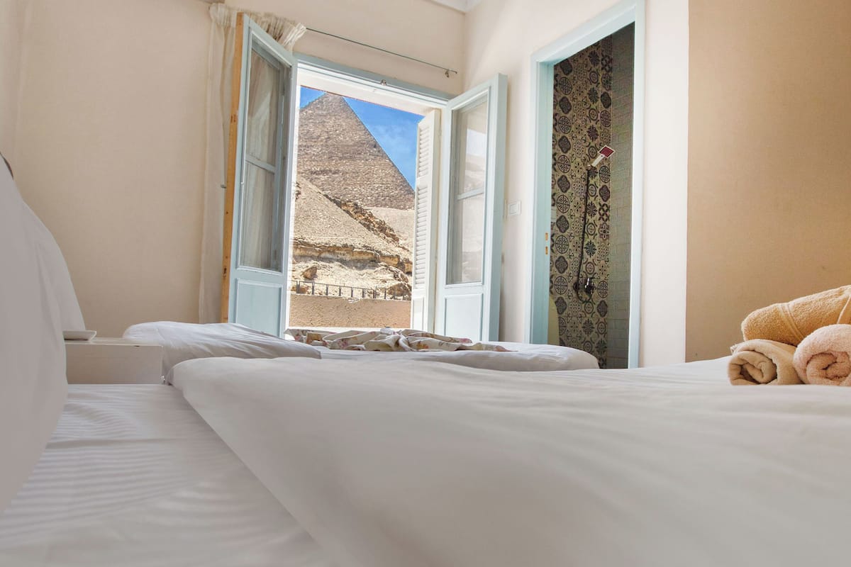 A hotel room with a bed, a window, and a view of a pyramid.