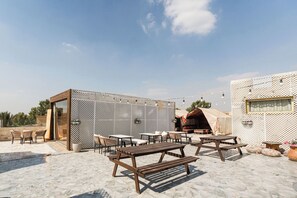 An outdoor seating area with wooden tables and benches, a decorative fence, and a tent-like structure. - Villa Khufu Pyramids Hotel (Giza)