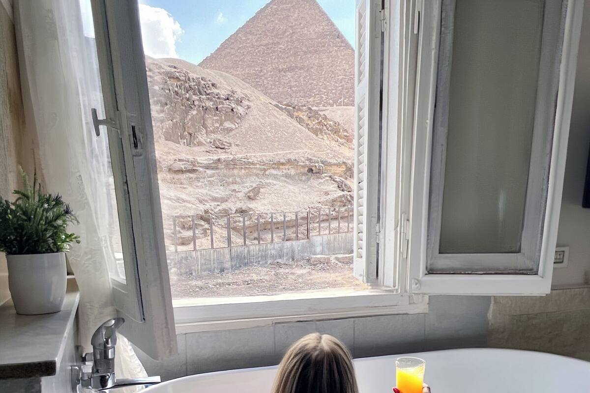 A bathtub with a view of a pyramid through an open window.