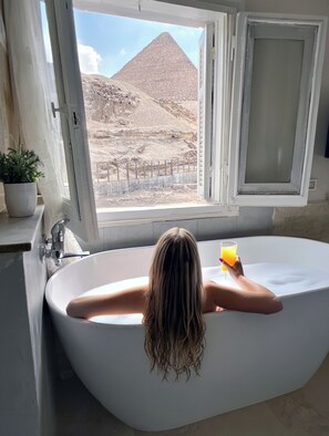 A bathtub with a view of a pyramid through an open window. - Villa Khufu Pyramids Hotel (Giza)