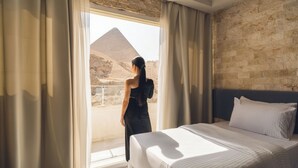 A hotel room with a large window, a bed, and a view of a pyramid. - Villa Khufu Pyramids Hotel (Giza)