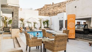 A poolside area with wicker furniture, a QR code for a mobile app, and a view of a rocky hillside. - Villa Khufu Pyramids Hotel (Giza)