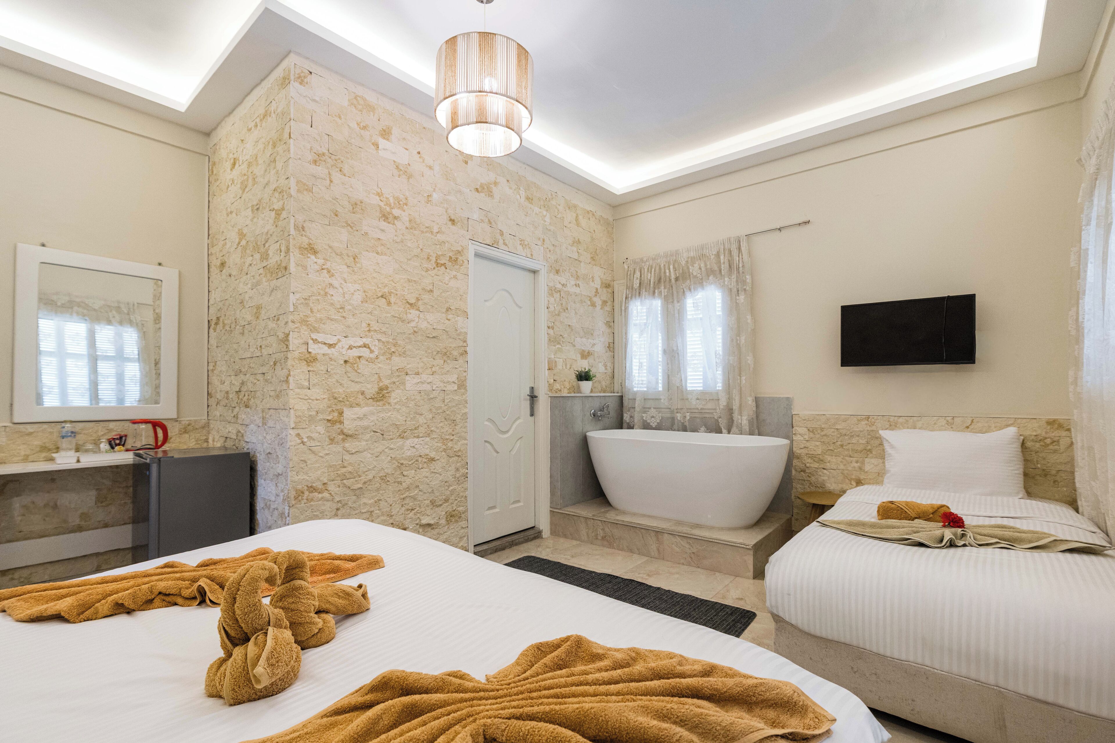 Une chambre d’hôtel avec un mur en pierre, une baignoire, un téléviseur à écran plat et deux lits avec des serviettes.