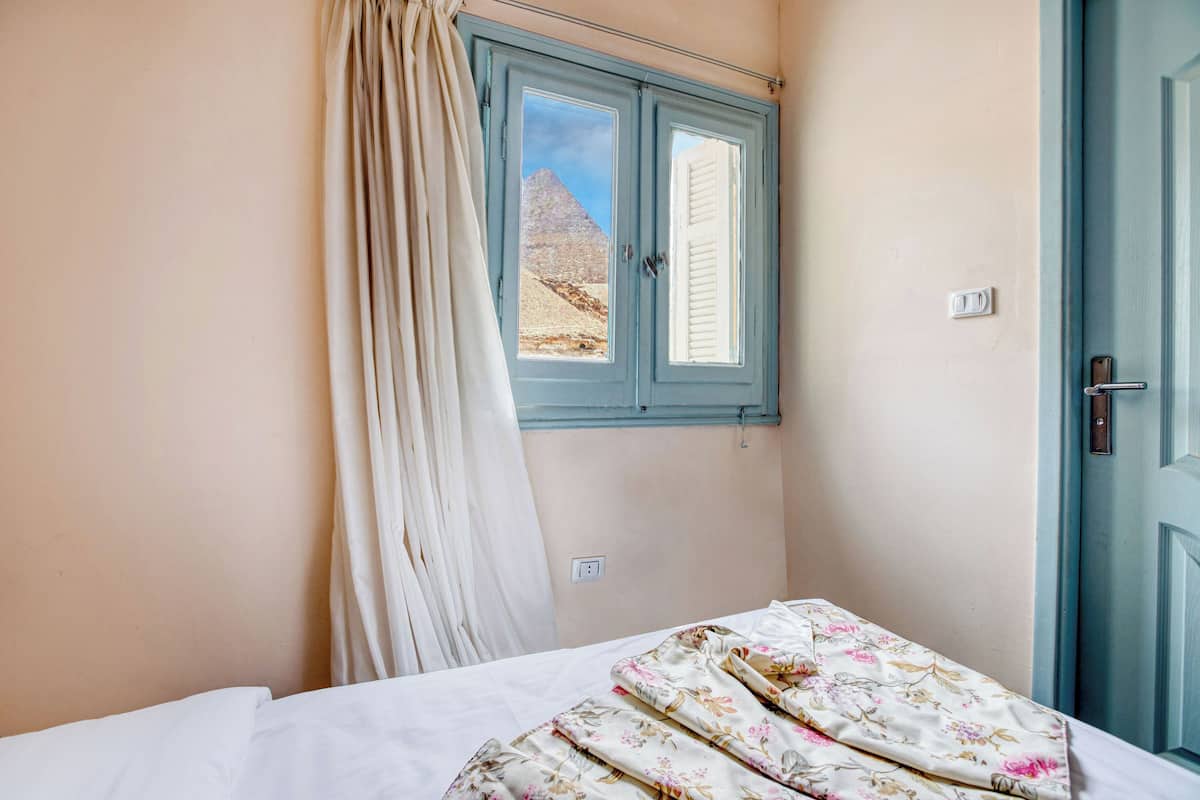 A bedroom with a bed, a window with a view of a mountain, a door, and a light switch.