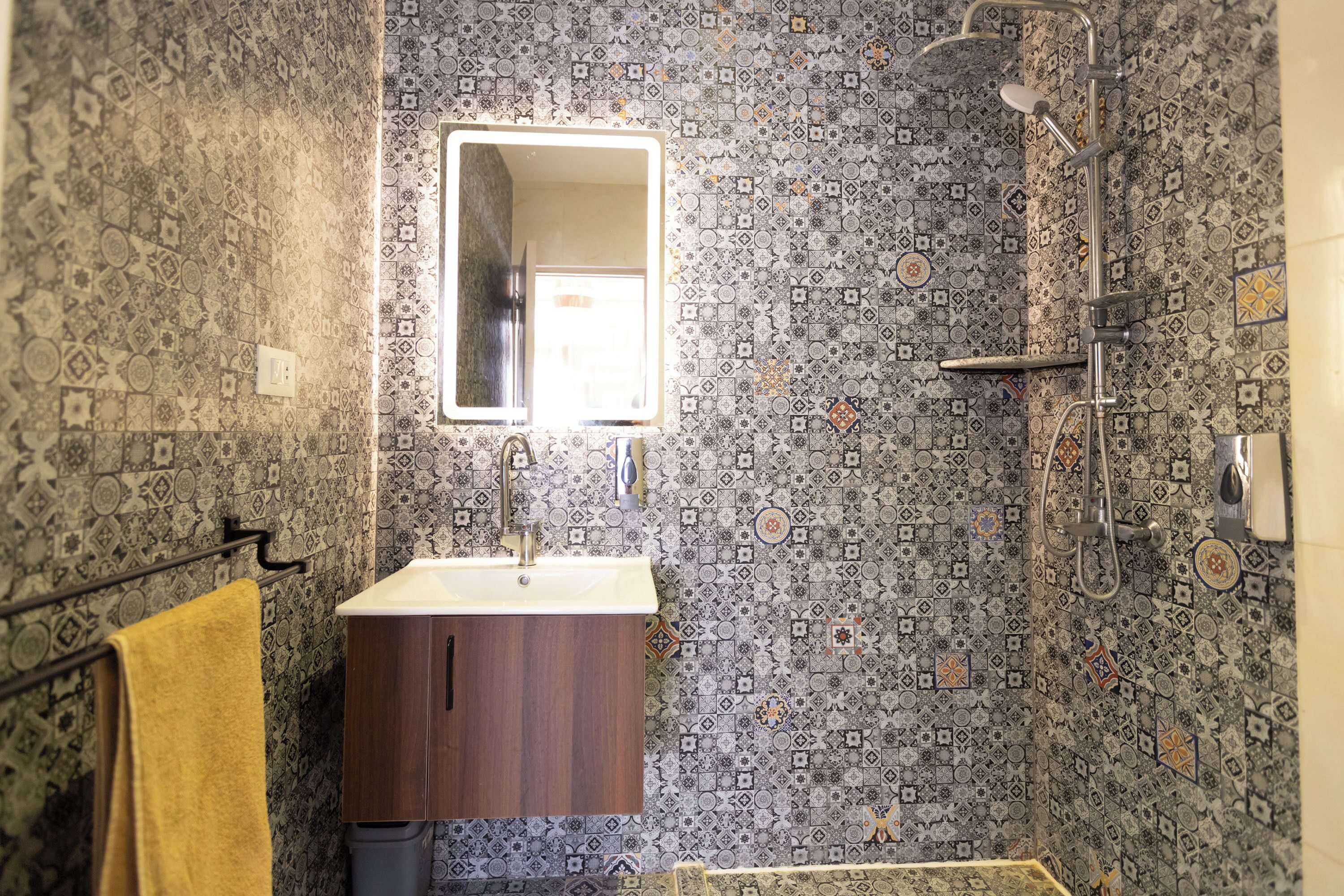 A bathroom with patterned tiles, a sink, a mirror, and a shower.