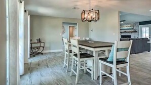 Un comedor con una mesa de madera y sillas blancas, un candelabro y una cocina al fondo.