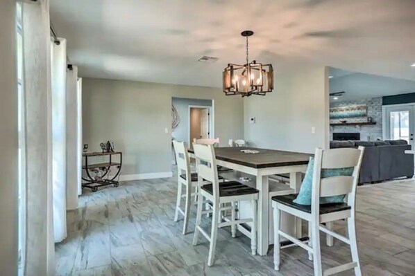 A dining area with a wooden table and white chairs, a chandelier, and a kitchen in the background. - Cozy Safety Harbor Retreat w/ Heated Pool & Near Downtown (Safety Harbor)