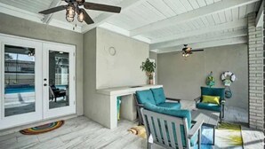 Un patio amplio con ventilador de techo, puerta corrediza de vidrio que da a una piscina y un área de estar con mesa y sillas.
