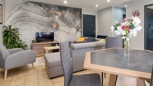 Un salon moderne avec un canapé gris, une table à manger et un téléviseur posé sur un meuble.