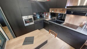 Une cuisine moderne avec des meubles de rangement aux couleurs sombres, un four encastré, un lave-vaisselle et un plan de travail en granit.