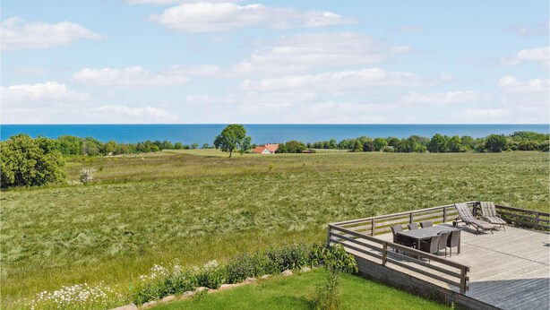 A grassy field with a wooden deck, a table, and chairs. - 3 bedroom cozy home in østermarie (Østermarie)