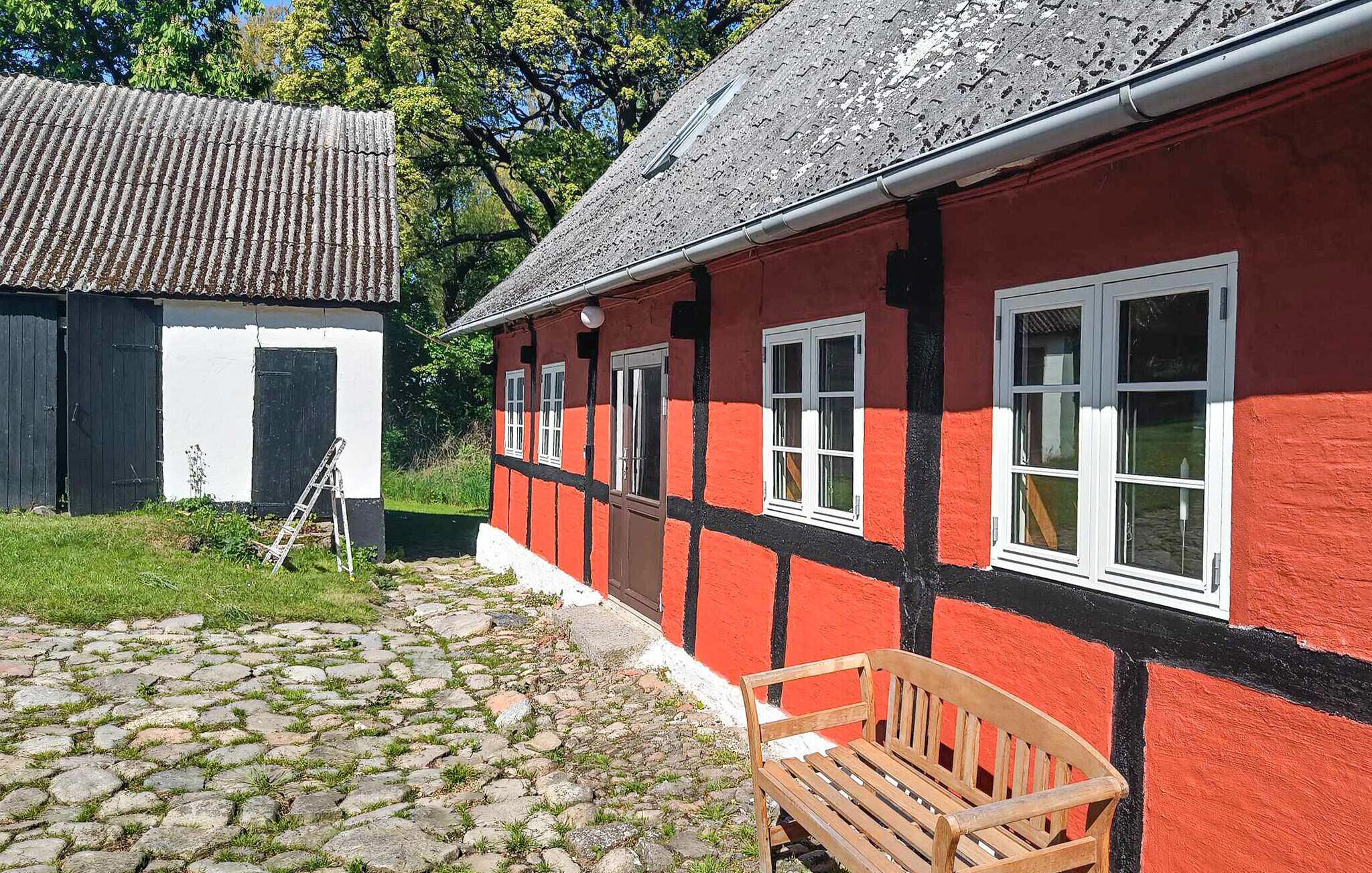 A traditional building with a red exterior and black trim, a cobblestone path, and a wooden bench.