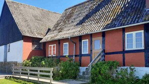 A traditional house with a steeply pitched roof, a wooden staircase leading to the entrance, and a small wooden fence in the foreground. - 3 bedroom cozy home in østermarie (Østermarie)