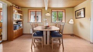 A dining area with a round table, wooden chairs, and a bookshelf. - 3 bedroom cozy home in østermarie (Østermarie)