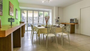 A dining area with a table set for four, white chairs, a wooden counter, and a view through a glass door to an outdoor area with a stone wall. - Beautiful home in Mascalucia (Mascalucia)