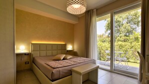 A bedroom with a bed, bedside lamps, a bench, and a view of greenery through large windows. - Beautiful home in Mascalucia (Mascalucia)