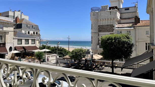 A coastal cityscape with historic buildings, a beach, and a café with outdoor seating.
