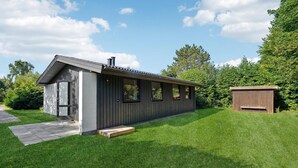 Een modern, gelijkvloers huis met een schuin dak, schoorsteen en een klein bijgebouwtje.