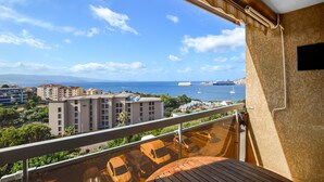 Un balcón con vista al mar, edificios y coches aparcados.