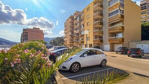 Un edificio residencial de varios pisos con balcones, coches aparcados y cielo despejado.