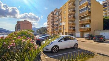 Un immeuble résidentiel à plusieurs étages, doté de balcons, avec des voitures garées et un ciel dégagé.