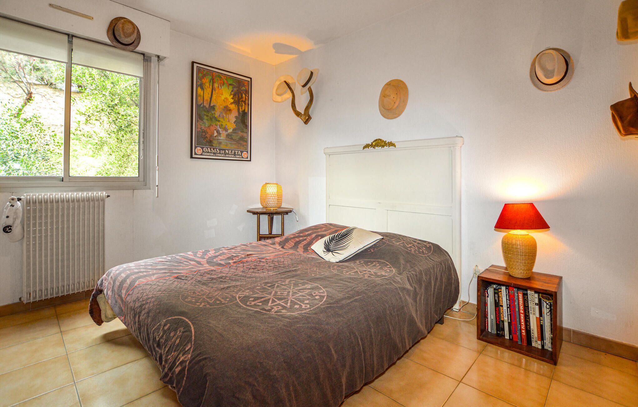 A bedroom with a bed, a radiator, a window, a painting, and a bookshelf.