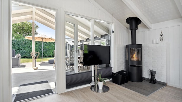 Ein modernes Wohnzimmer mit Kamin, Fernseher und einer Terrasse mit Gartenmöbeln.